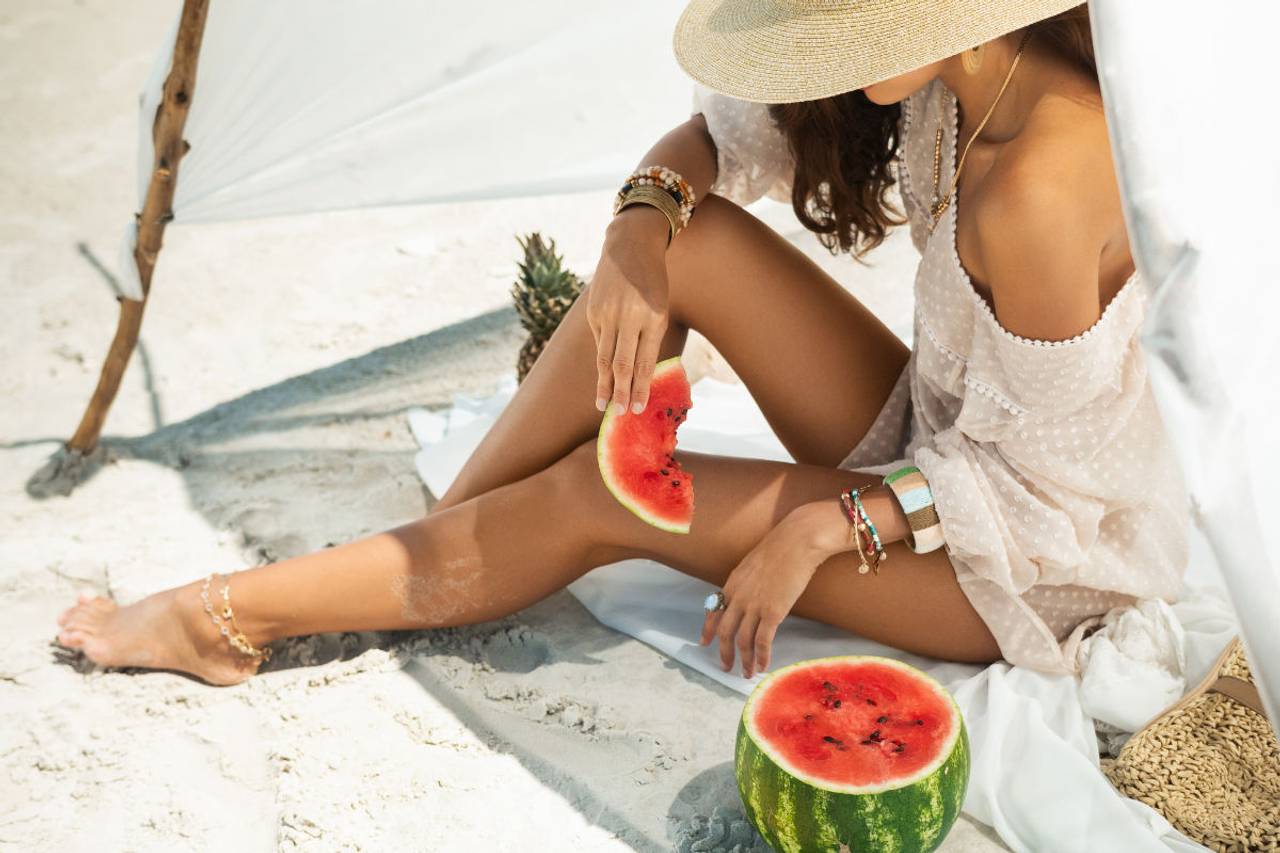 mulher sentada na areia comendo melancia 