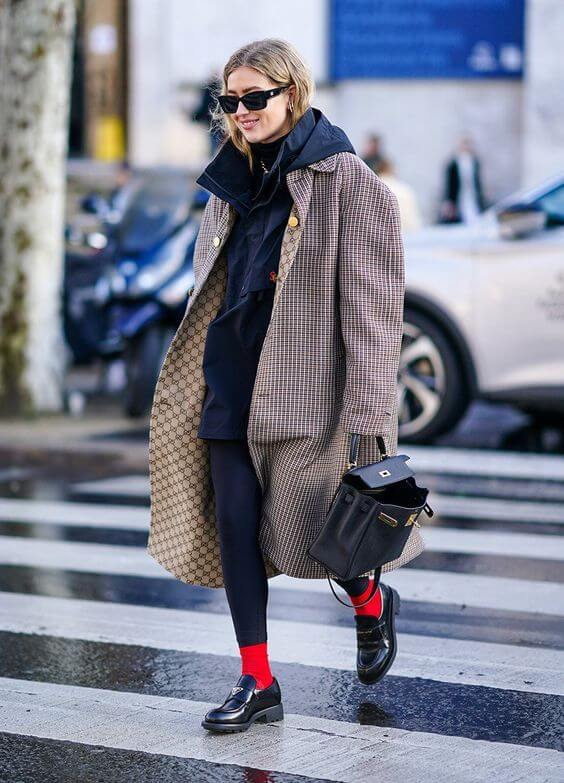 mulher caminhando com look com mocassim, calça legging preta, casaco xadrez e meias vermelhas.