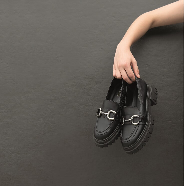 Mãos femininas segurando sapato loafer preto