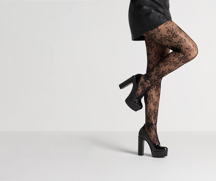 Pernas femininas usando meia-calça preta e sapatos de salto preto.