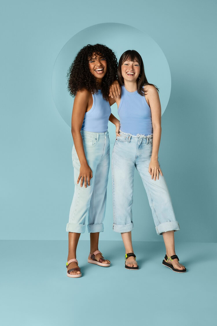Duas mulheres vestidas de azul claro em um fundo azul claro e usando sandálias Zaxy+Gabriela